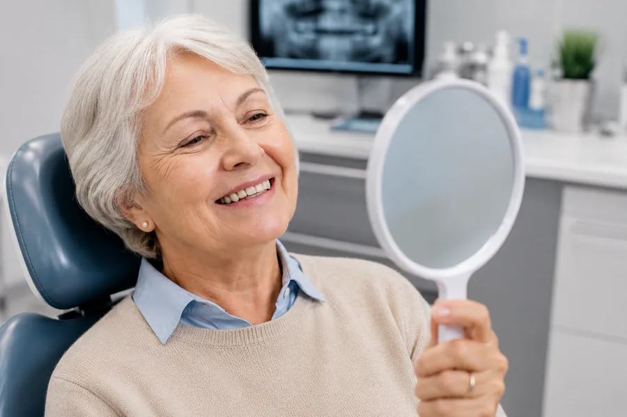 Happy patient admiring her restored smile in a mirror at Southern Pines Family Dental